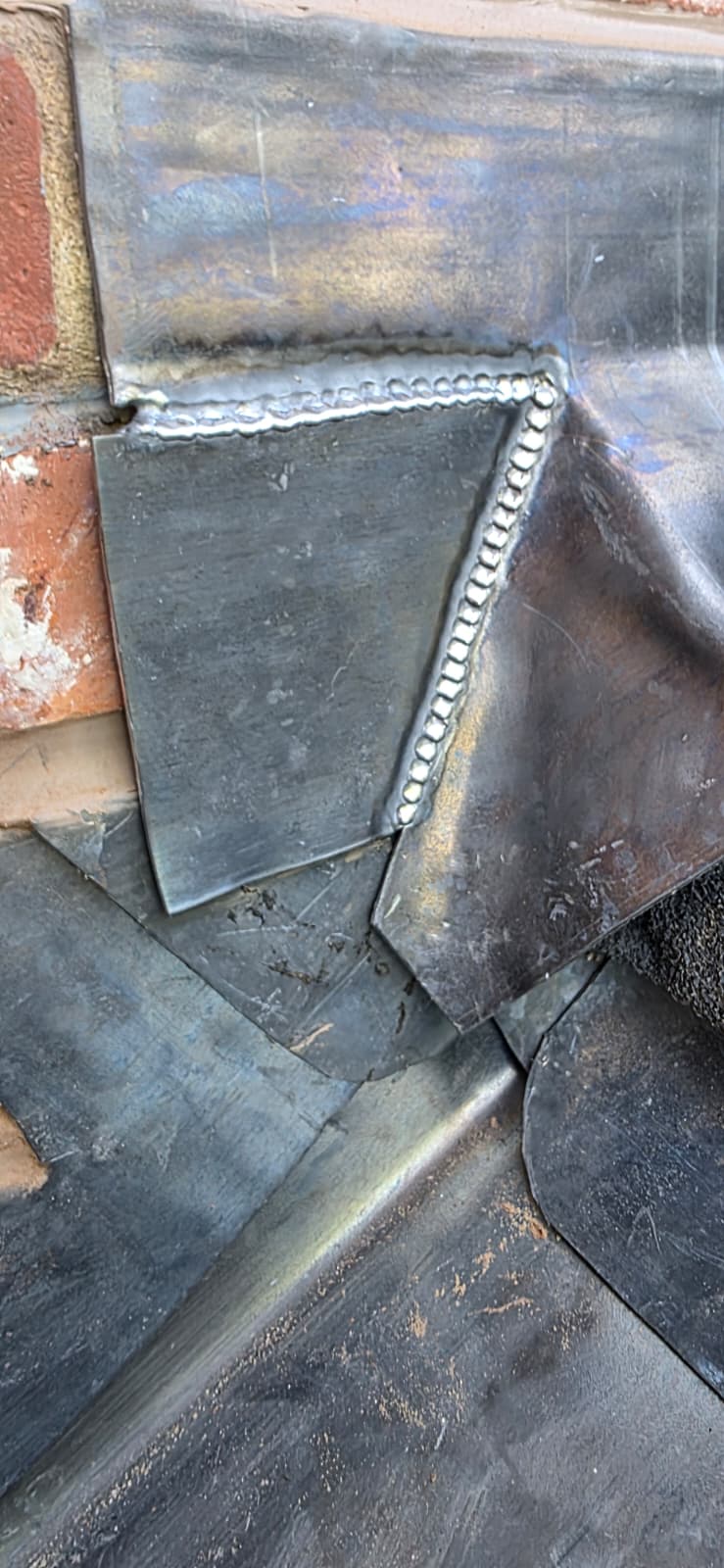 Close-up of lead-welded soaker seams against brickwork